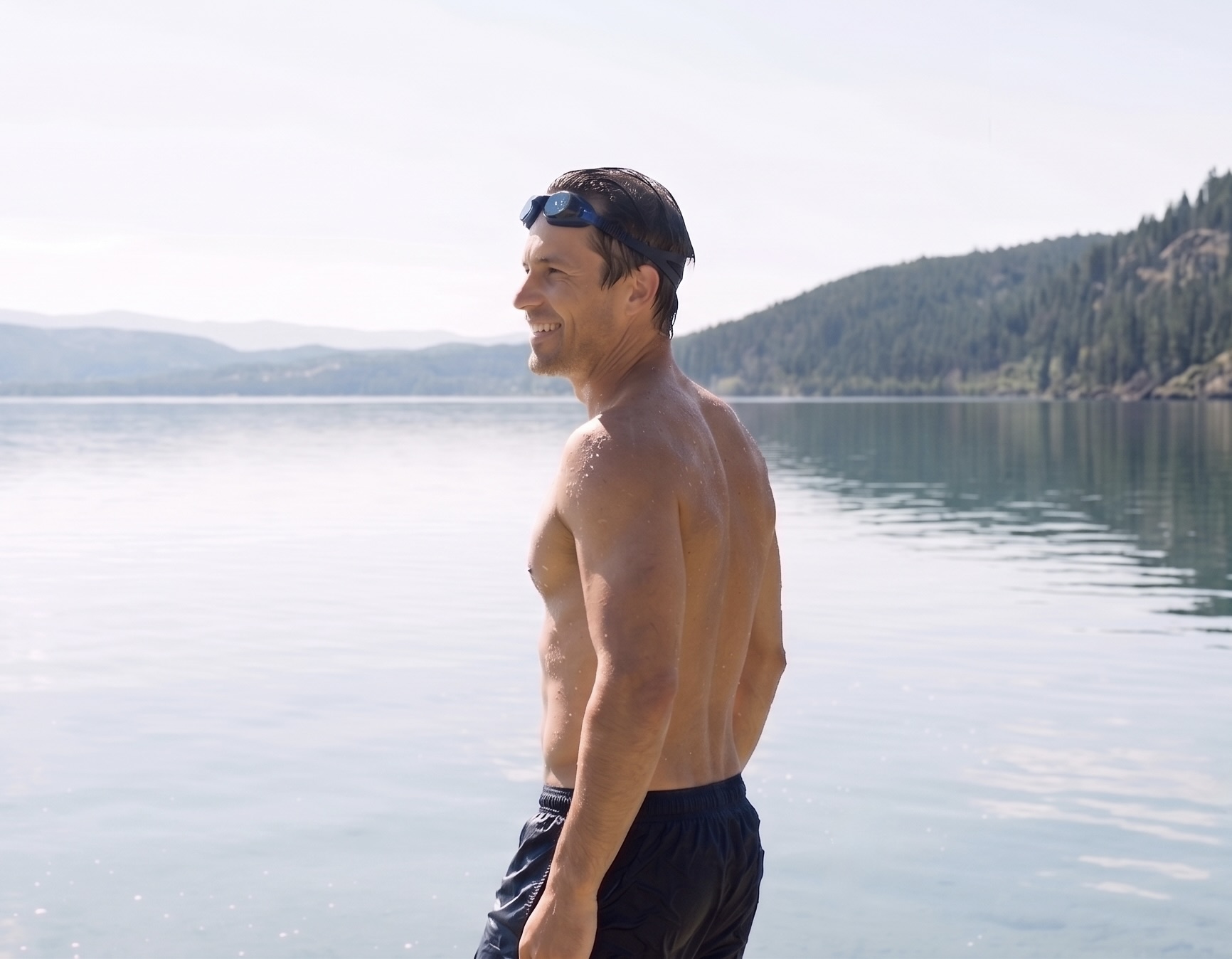 A fit, smiling swimmer standing in a calm lake after a swim